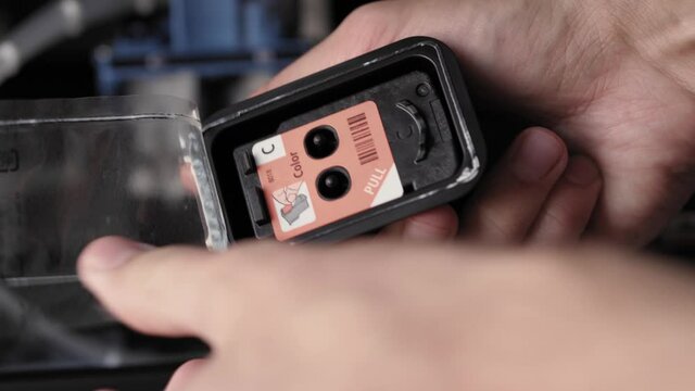 Video instruction, technology, press, media, office, stationery concept - close-up of male hands preparing new inkjet printer for launch. step 2: remove protective label from cartridge filling holes