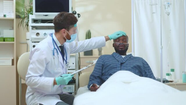 Professional doctor measuring temperature touching forehead of african american sick patient in hospital room. Health, medical assistance. Hospitals.