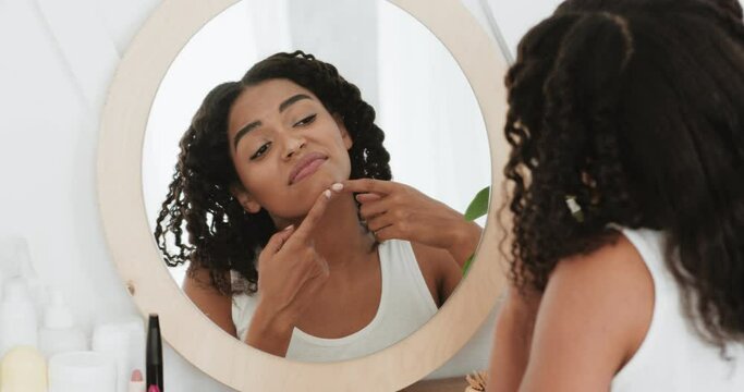 Problem skin concept. Sad african american lady looking at mirror and crushing pimple on her chin, back view