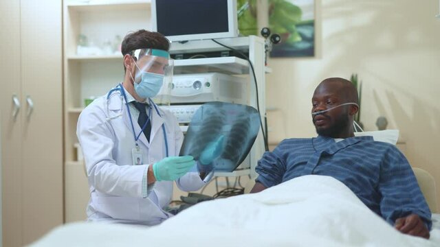 Professional caucasian adult physician treating unhealthy sick patient in hospital room showing xray image of lungs explaining disease symptoms. Coronavirus. Virus infection.