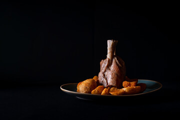Lam leg with potatoes on a black background © Vlad Chețan/Wirestock