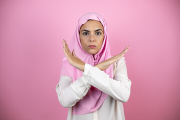 Young beautiful arab woman wearing islamic hijab over isolated pink background Rejection expression crossing arms doing negative sign, angry face
