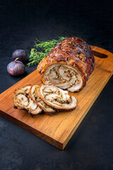 Traditional Italian Porchetta arrotolata pork meat sliced and as piece with herbs and figs offered as close-up on a modern design wooden board