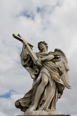 Vertical shot of the Bernini's marble statue of angel with cross from the St Angelo Bridge in Rome