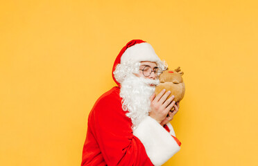 Fototapeta na wymiar Cute Santa Claus hugging a toy deer on a yellow background. Christmas and New Year concept. Santa and a plush toy