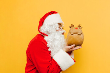 Funny Santa hugs a toy deer on a yellow background with closed eyes. Christmas and New Year concept.
