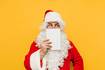 Fototapeta na wymiar Funny santa isolated on yellow background with book in hand, looking aside with serious face. New Year and Christmas.