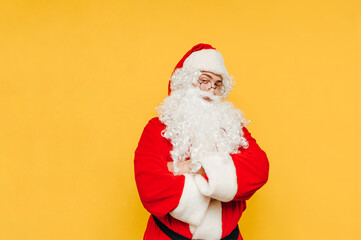 Happy man in santa claus costume stands on yellow background and looks at camera with smile on face. Isolated. Christmas and New Year