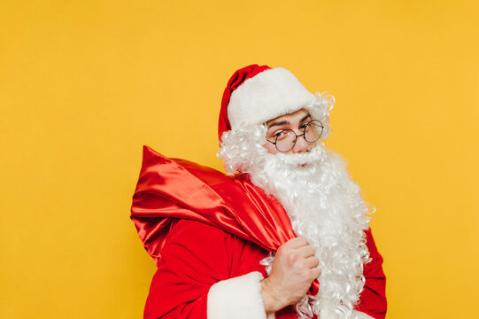 Portrait of Santa with a bag of gifts isolated on a yellow background, looking at the camera with a smile on his face. Christmas and New Year.