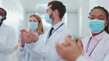 Multi-race professional medical doctors and assistants wearing protective masks against coronavirus applauding on team conference business employment meeting in corridor. Cooperation and success. - Powered by Adobe