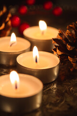 Several burning candles on a silver tray with pine cones and holly berries in the background