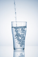 Fresh mineral water pouring into glass on blue background