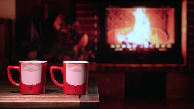 Mugs with the image of Santa Claus in front of the fireplace. Festive cozy Christmas or New Year mood.
