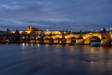 
Charles Bridge on the Vltava river and statues on it and lit street lights and light from lamps at night in the center of Prague in the Czech Republic and there are clouds in the sky