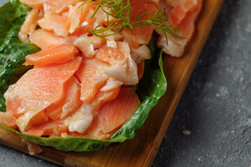 Pieces of fried salmon with dill and lemon wedges on a wooden board