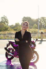 Obraz na płótnie Canvas Seductive young woman in tight fitting black suit poses near sport motorcycle at self service car wash.