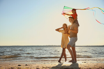 Happy parents and their child playing with kite on beach near sea. Spending time in nature