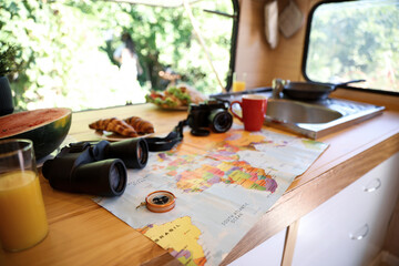 World map and travel accessories on wooden table in motorhome. Summer trip