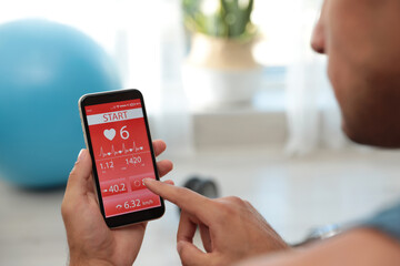 Man using fitness app on smartphone indoors, closeup