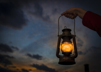 Female's hand holding a lantern with the beautiful sunset in the background © Samir Behlic/Wirestock