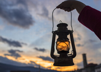 Female's hand holding a lantern with the beautiful sunset in the background © Samir Behlic/Wirestock