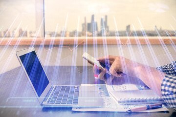 Double exposure of man's hands holding and using a digital device and forex graph drawing. Financial market concept.