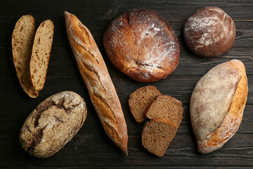 Different kinds of fresh bread on black wooden table, flat lay