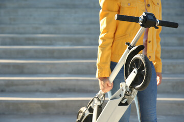 Woman carrying folded electric kick scooter outdoors, closeup. Space for text © New Africa