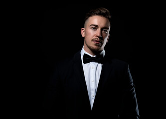 Handsome young man in suit and bow tie posing on black background