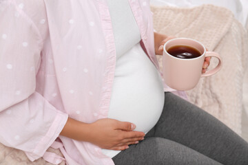 Pregnant woman drinking tea at home, closeup