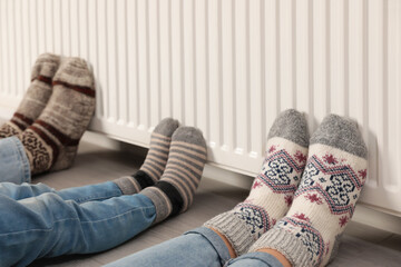 Family warming legs near heating radiator indoors, closeup