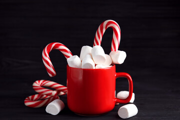 Cup of tasty cocoa with marshmallows and Christmas candy canes on black wooden table