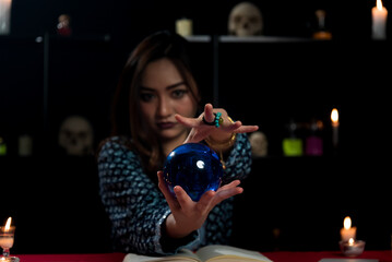 Portrait of Gypsy fortune teller woman in dark room with blue crystal ball. Focused on hand.