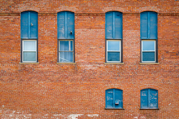 Exterior Wall of an Old Orange Brick Building with Windows and Blue Shutters