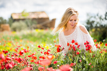 Naklejka premium Beautiful young female in white dress in poppy field of wild flowers outdoor
