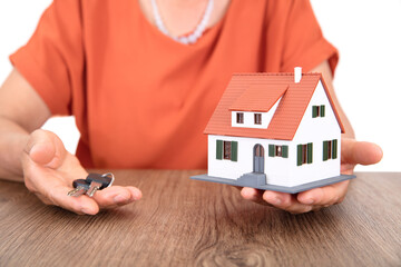 The old Chinese lady is holding a small house model in one hand and the new house key in the other...
