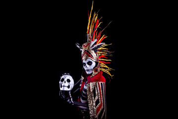 hombre latino , catrin de dios azteca, calavera prehispanica, con saumerio e incienso y fuego, portado penacho de plumas amarillas y rojas en fondo negro, dia de muertos, 1 de noviembre, calaca,
