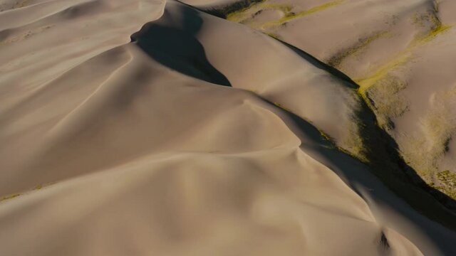 Aerial view tilting over a sandbanks, revealing the North Zapata mountain ridge in background, in the Great sand dunes national park - tilt up, drone shot