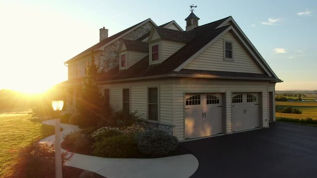 Dramatic sunrise illuminates large stone farm house with green front yard. Morning, wake up, new beginning theme. Aerial truck shot.
