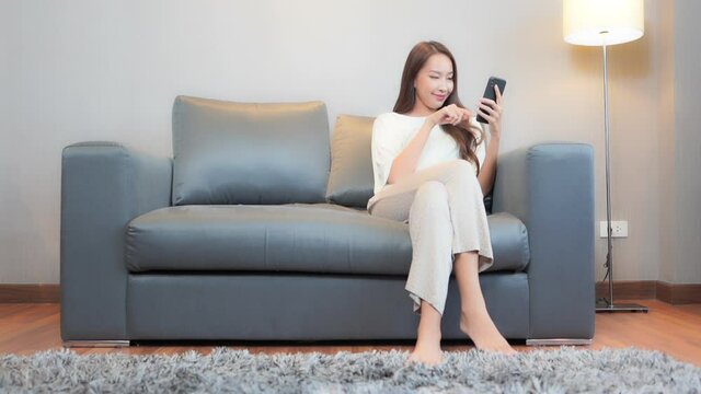 While sitting on a comfortable grey leather couch a pretty young woman focuses on her smartphone as she inputs her next text.