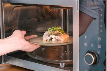 A housewife steaming fish in a microwave oven for a family dinner. She prepares it by putting fish...