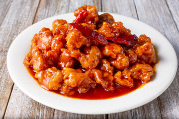 A view of a plate of spicy orange chicken, in a restaurant or kitchen setting.