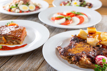 A view of several Italian plates on the table featuring roasted polletto, eggplant parmigiana and caprese.
