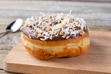 A view of a chocolate glazed donut, featuring shredded coconut toppings, in a restaurant or kitchen setting.
