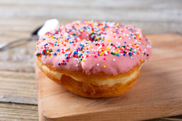 A view of a pink frosted donut with rainbow sprinkles, in a restaurant or kitchen setting.