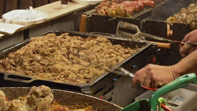 Cooking cabbage with meat in a cauldron. A man mixes Bigos, a traditional Polish dish. Fast food, outside. Festival of flavors. Fest.
