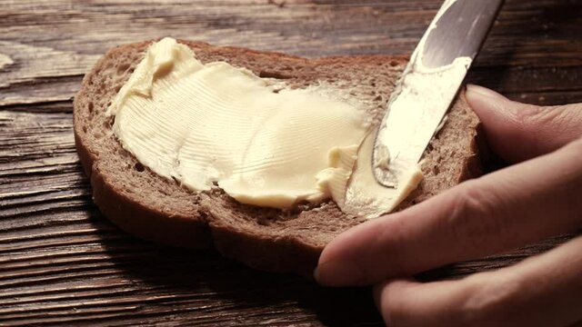 Close-up butter spreading on rustic rye bread with metal knife on wooden table