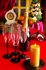 Four glasses of champagne, a bottle, a burning candle on a table with a red tablecloth