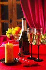 Two glasses of champagne, a bottle, a burning candle on a table with a red tablecloth