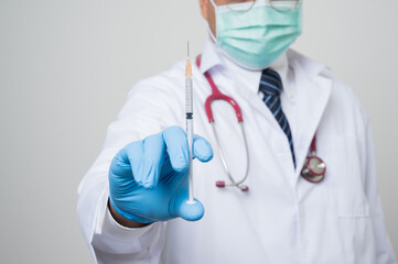 Close Up Asian bald Doctor in white coat, stethoscope, blue glove showing a.syringe in front of camera isolated on white background.